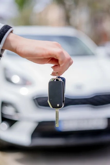 Hand holding a car key in front of a white vehicle representing car purchase and insurance in Portugal